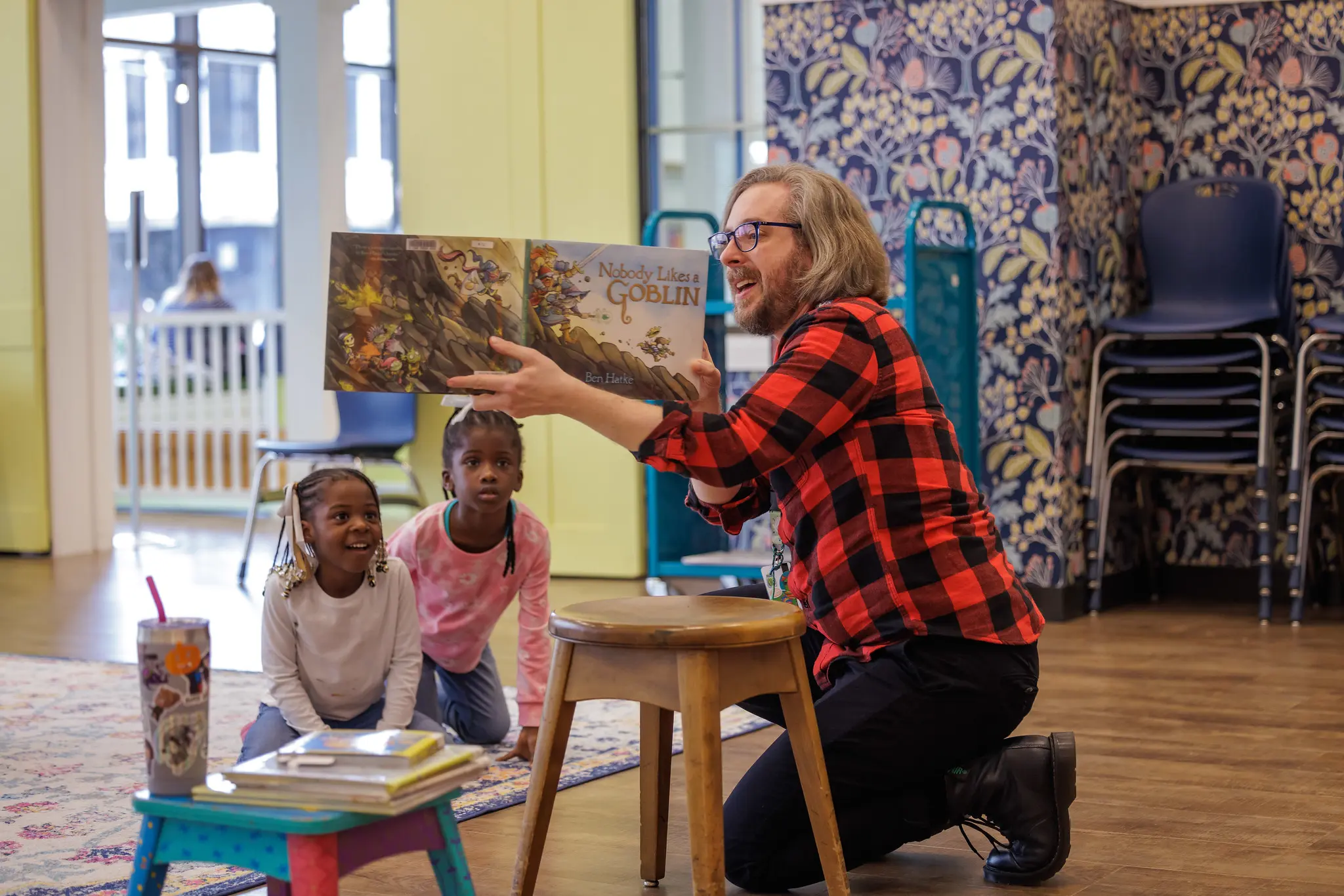 A librarian reading a story book to two children who are very into the story being read.