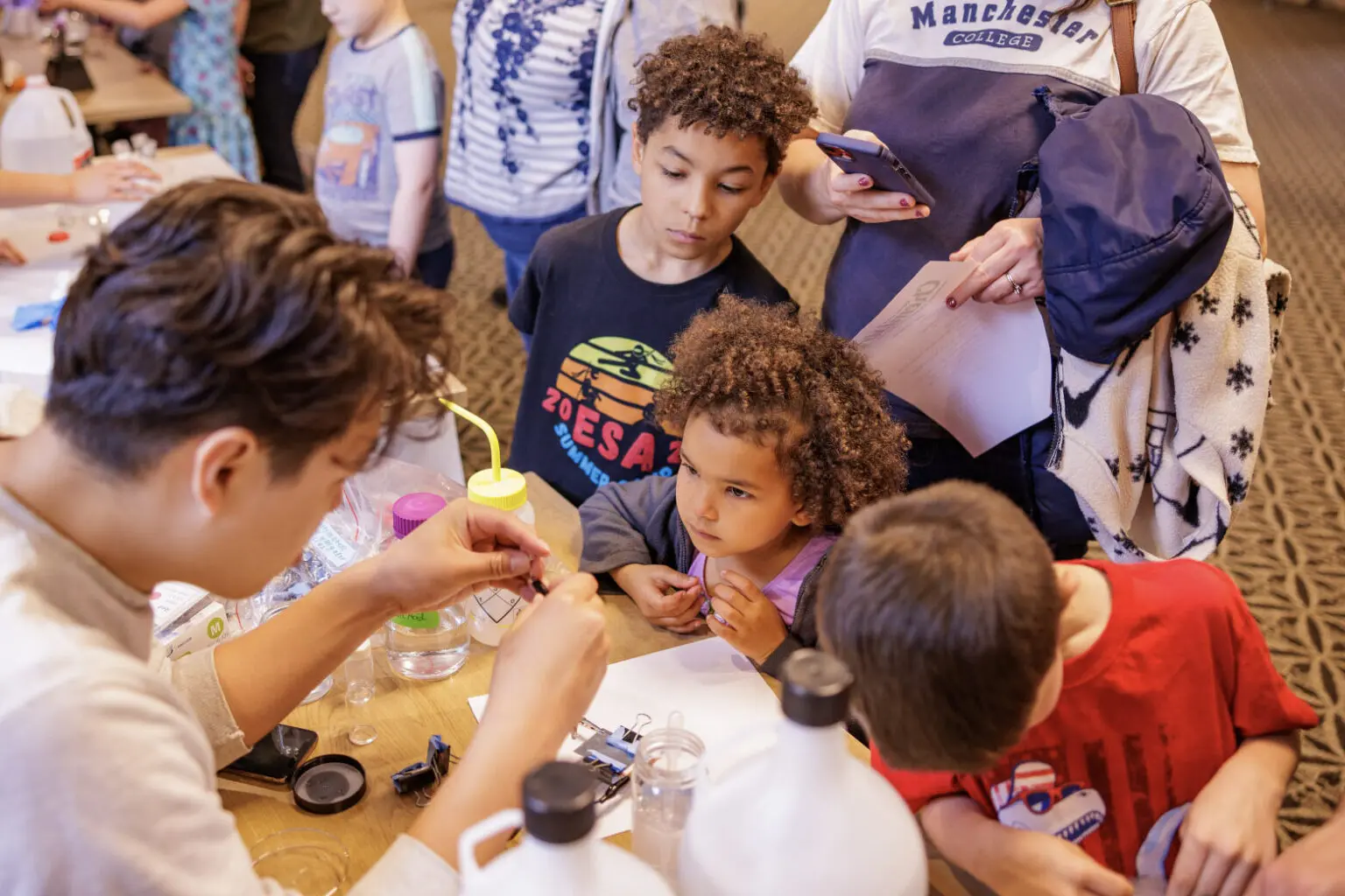 A group of children gather around a table, experimenting with colorful liquids and tools during a hands-on activity.